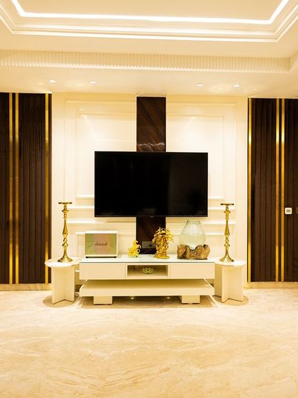 The TV wall in this living room is designed to be both functional and beautiful, with dark wood panels and gold inlays that conceal storage and frame the screen.