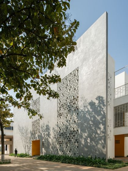 The facade of Vidyashilp Academy features large 'jali'-inspired panels that filter sunlight and maintain constant airflow. This passive design strategy, combined with the preservation of existing trees, creates a climate-responsive and energy-efficient learning environment.
