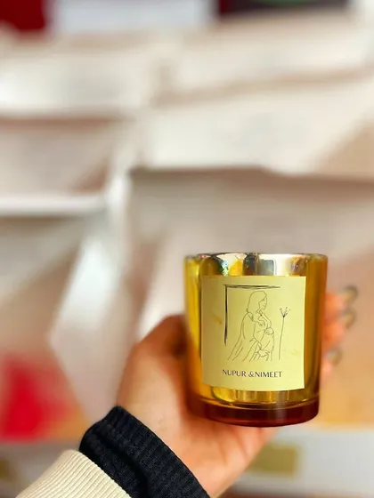 A handheld view of the metallic jar candle included in our baby shower hampers. The custom label with the parents' names adds a deeply personal touch.