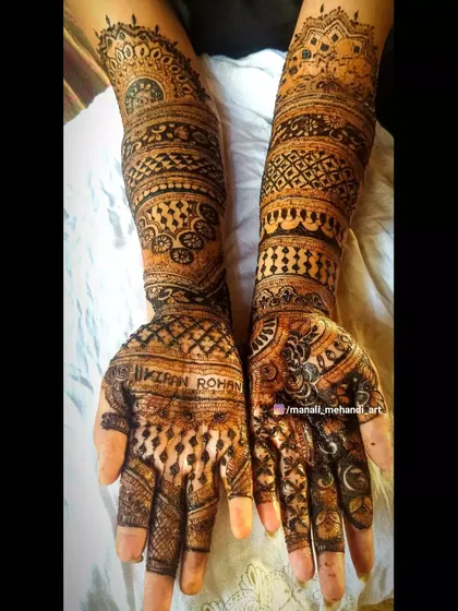 The back of the hands for a bridal design, featuring the names 'Kiran' and 'Rohan' on the palms. The pattern is a mix of jaal work and bold floral elements.