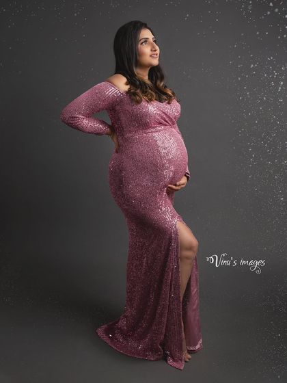 A glamorous profile shot in a shimmering pink gown. The pose accentuates the beautiful curve of her baby bump, creating a sophisticated and stylish maternity portrait.