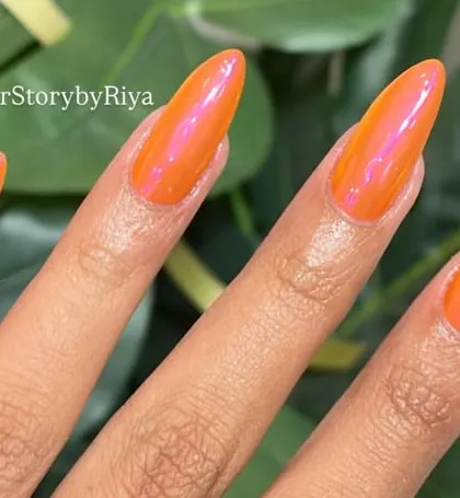 Vibrant orange chrome nails that are impossible to ignore. These long, stiletto nails have a stunning pink iridescent shift under the light, perfect for making a bold and summery statement.