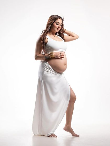A graceful and strong pose. This black and white studio portrait in a white outfit highlights the beauty and power of the pregnant form with clean, high-contrast lighting.