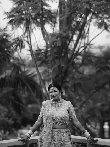 A black and white outdoor portrait of a bride on a balcony, with a beautiful tree in the background.