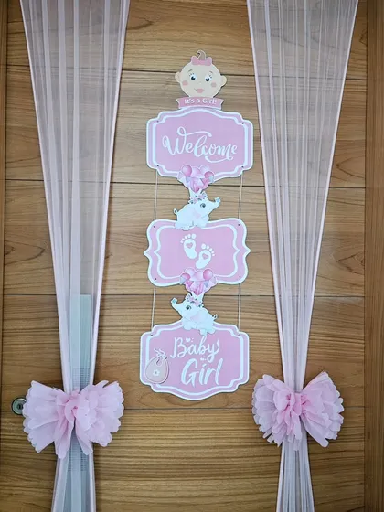 A 'Welcome Baby Girl' door decoration. The pink signs, sheer curtains, and bows create a beautiful and delicate entrance to celebrate the new arrival.