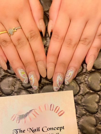 A soft and artistic design on long, almond-shaped nails. The nude base is enhanced with accent nails featuring a delicate, paisley-like pattern in white and gold.