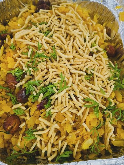 A takeaway container filled with our delicious poha, garnished with fresh coriander and crunchy sev. A perfect breakfast or light snack.
