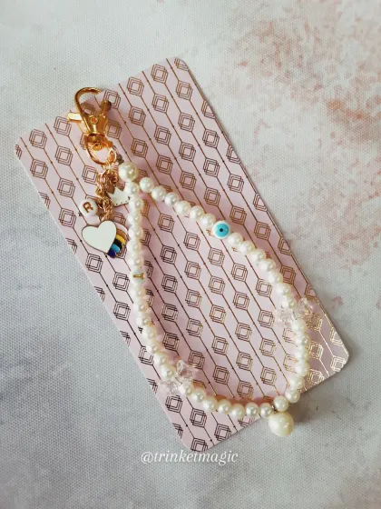 Another view of the custom pearl phone charm, displayed on its backing card. The combination of personal initials and protective symbols makes it a truly meaningful gift.