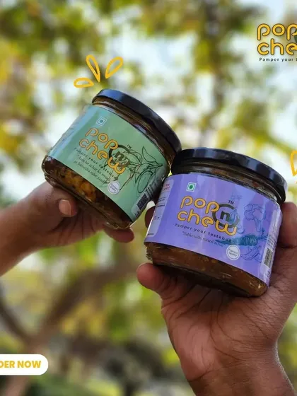 Two of our most loved flavours, the mixed vegetable and garlic pickles, held up for you to see. This image captures the vibrant colours and the excitement of choosing your favourite jar.