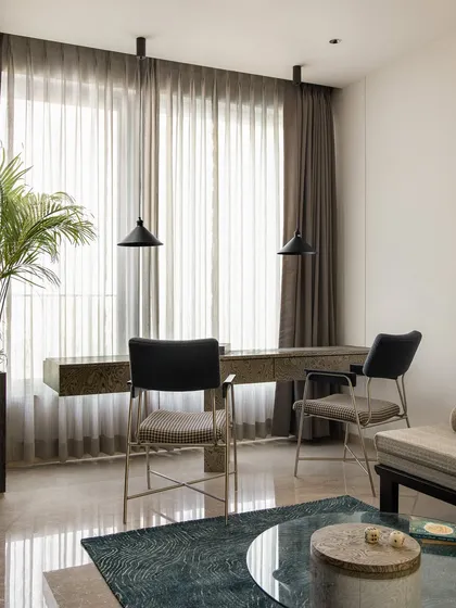 The workstation in the multipurpose room, featuring a floating desk and chairs set against a large window. A tall planter adds a refreshing touch of nature to the space.