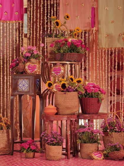 A beautiful photo corner at the Haldi, featuring a tiered arrangement of stools with flowers in wicker and jute baskets, set against a backdrop of floral strings.
