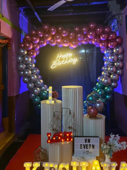 A first birthday decoration done in a home setting. We used a multi-color chrome balloon arch, ribbed stands, and marquee letters for the name 'KRISHNAYA' to create a festive photo corner.