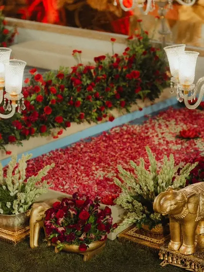 A pathway leading to the mandap, lined with rich red rose petals and elegant brass elephant statues. The combination of floral beauty and traditional metalwork creates a luxurious and welcoming walkway.