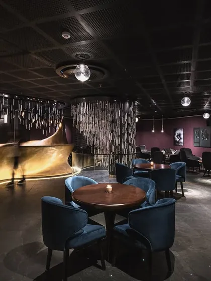 This lounge interior in our 'Moody Blues' project transforms the space into a fluid work of art. The design uses a dark, intimate color palette with plush blue velvet chairs and a dynamically lit, curving bar to evoke a sense of freedom and movement.