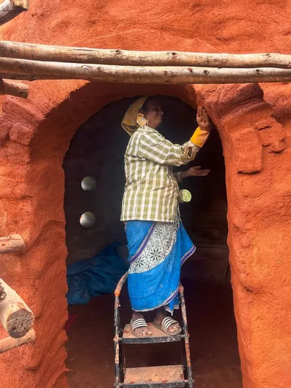 A woman mason applies the finishing touches to a mud wall at Cheerville. Her grace and strength are woven into the very fabric of the building.