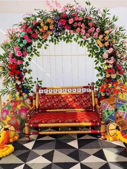 This is what a proper Mumbai Haldi ceremony should feel like. We used a full arch of multi-colored flowers to create a vibrant backdrop, complemented by a traditional red and gold seat, decorative umbrellas, and marigold arrangements. It’s a perfect photo spot for the bride or groom.