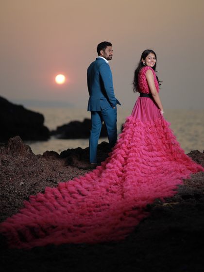 A stunning sunset pre-wedding shoot. The long, ruffled train of this pink gown creates a dramatic silhouette against the evening sky.