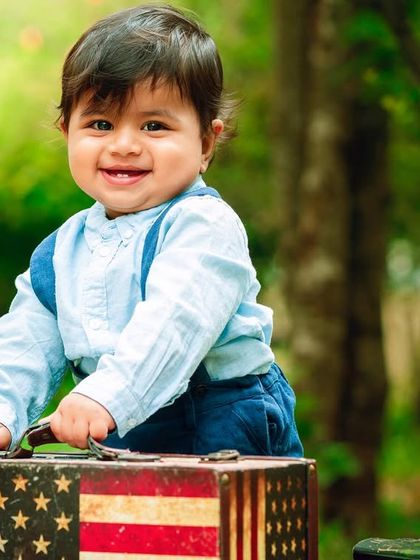 A big, proud smile from our little explorer. The American flag suitcase adds a fun, graphic element to the shot.