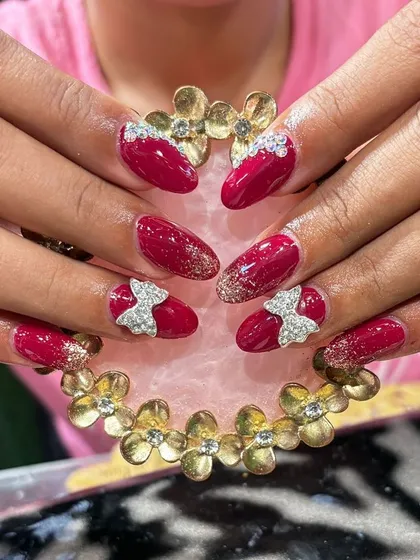 A bold magenta nail set featuring sparkling silver 3D bows and a dusting of gold glitter for a fun, high-contrast look.