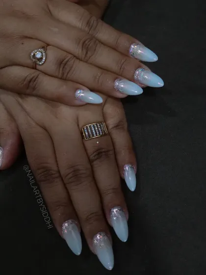 A set of long, almond-shaped extensions with a milky blue base and silver glitter French tips.