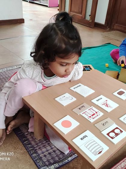 In our classroom, children learn to write before they learn to read. This image shows a child using picture and word cards with the movable alphabet, an intuitive approach that taps into a child's natural desire to create.