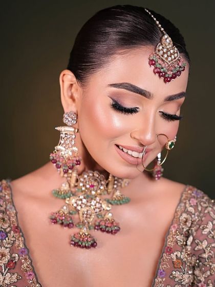 A smiling bride wearing an elaborate navratan style polki necklace with matching oversized earrings and maang tikka. The mix of colours makes it versatile for many outfits.