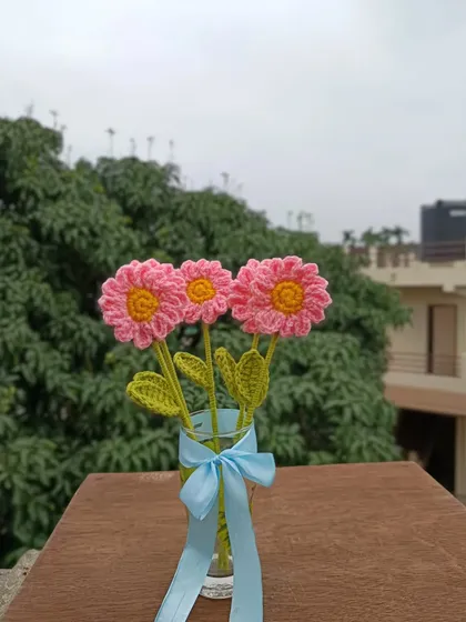 A small vase of pink daisy stems with a blue ribbon.
