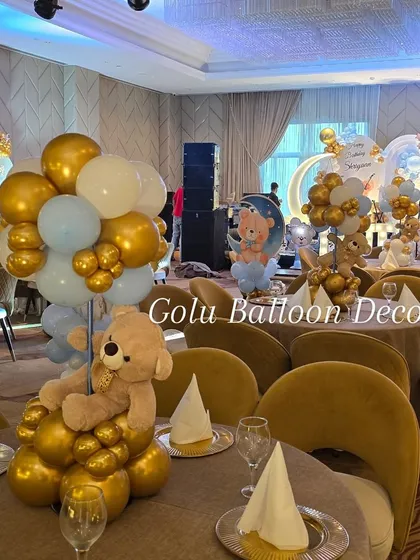 A teddy bear themed table centerpiece, with a plush bear sitting on a base of gold and blue balloons.