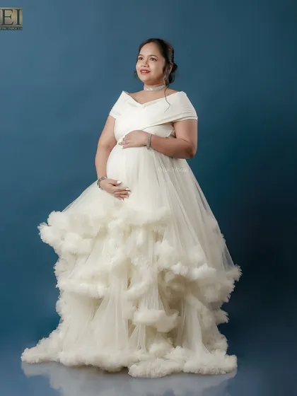 An angelic portrait in a voluminous white ruffled gown against a deep blue studio backdrop, creating a cloud-like effect.