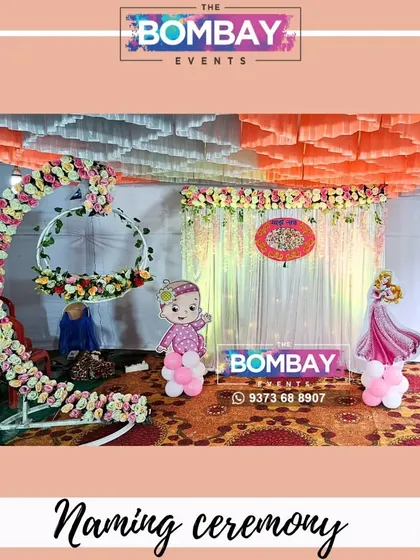 A full view of a traditional naming ceremony stage, complete with a floral cradle arch, backdrop, and cute baby character cutouts.