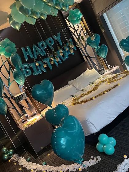 The dark green theme continues with "Happy Birthday" foil balloons and heart-shaped balloons over a bed scattered with gold petals.