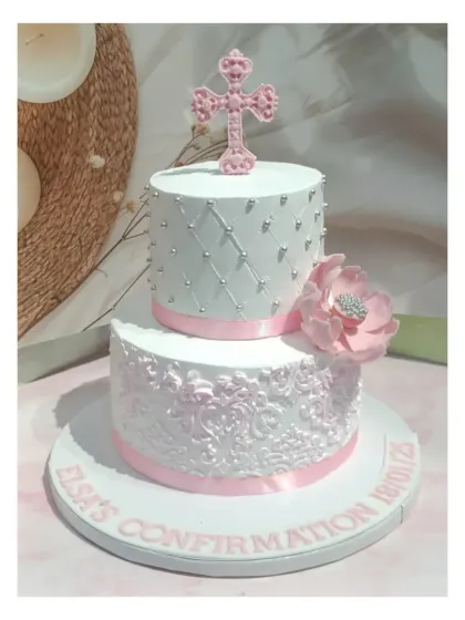 A beautiful two-tiered confirmation cake with a unique offset design. It features intricate lace work and a delicate pink cross and flower.