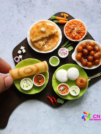 A close-up of a South Indian breakfast platter, complete with idli, vada, dosa, and kesari.