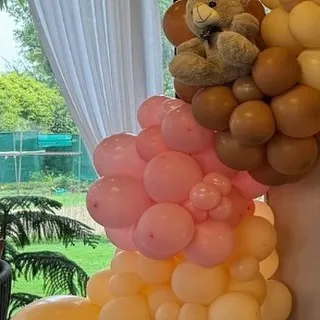 A teddy bear appears to be climbing a column of pink and brown balloons, adding a playful and dynamic element to the decor.