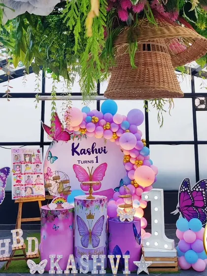 A stunning butterfly-themed first birthday party on a rooftop. This outdoor setup features a beautiful balloon arch, large butterfly props, and a 'ONE' marquee table, all complemented by hanging greenery for an enchanting garden feel.
