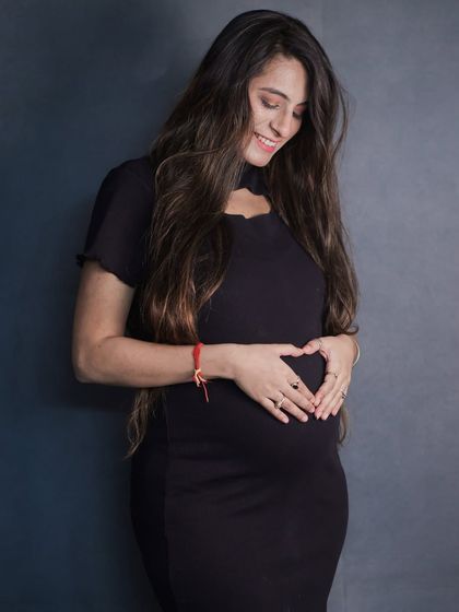 A simple, heartfelt pose. The mom-to-be makes a heart shape with her hands over her baby bump, captured with soft lighting against a dark, simple backdrop.
