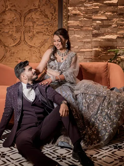 A stylish couple portrait for their reception. The bride is in a stunning grey lehenga with intricate floral embroidery, and the groom is in a dapper purple tuxedo.