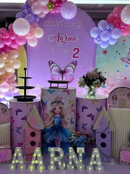 A close-up of the butterfly-themed cake table area, showing the detailed graphics on the plinths and the light-up name display.