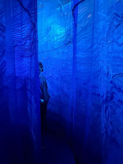A person immersed in the blue light of the 'Into The Deep' installation. The piece is an abstracted, poetic expression of the sea, using material, color, and sound.