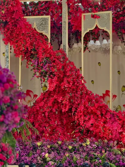 A cascade of red flowers flows down a mirrored arch, creating a dramatic and artistic floral installation that is a true statement piece.