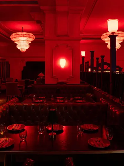 A large communal table, perfect for groups. The tufted leather banquette and dramatic chandeliers create a sense of occasion.