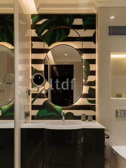 This bathroom vanity evokes a sense of luxury with premium materials and warm, integrated lighting. The elliptical mirror with its sleek frame is set against a bold backdrop of botanical prints and stripes, adding refinement and creating a serene retreat.