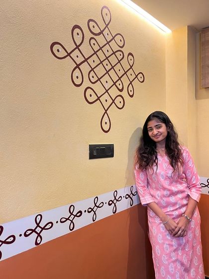Standing proudly next to the completed traditional rangoli wall art. The combination of the larger motif and the delicate border pattern creates a balanced and beautiful design for the entrance.