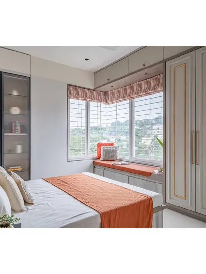 A cozy and modern guest bedroom featuring a comfortable window seat with storage underneath. The warm terracotta and grey color scheme creates an inviting atmosphere.
