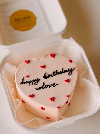 A lovely pale pink, heart-shaped bento cake with "happy birthday love" in black script, perfect for a significant other.
