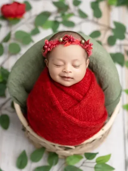 A peaceful, smiling newborn in a basket, surrounded by green leaves and red roses.