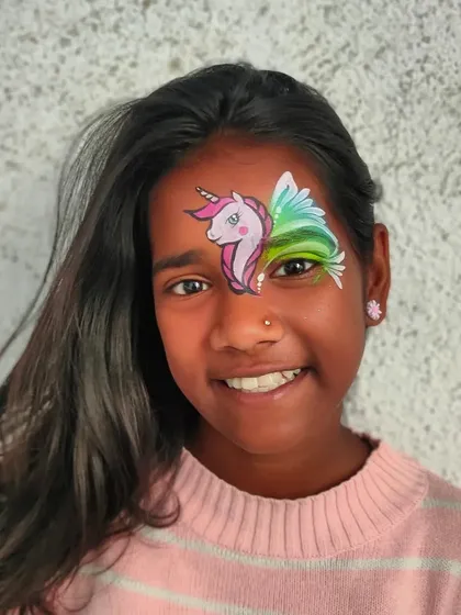 A smiling girl with a winged unicorn face paint, looking absolutely magical.