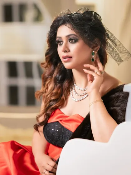 A glamorous, old-Hollywood inspired portrait. The model's elegant red and black gown, diamond necklace, and veiled fascinator create a look of timeless sophistication.