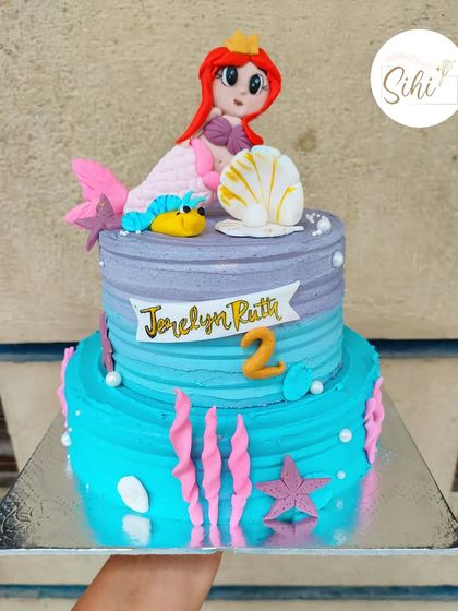 An under-the-sea adventure with this Little Mermaid cake. The two-tier design in shades of blue and purple features a fondant Ariel, a fish, and other ocean-themed details.