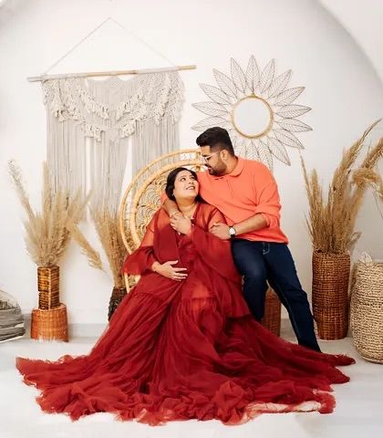 A wide shot of a boho-themed studio session. The expecting mother is seated in a peacock chair, surrounded by natural elements, creating a warm and inviting pregnancy portrait.